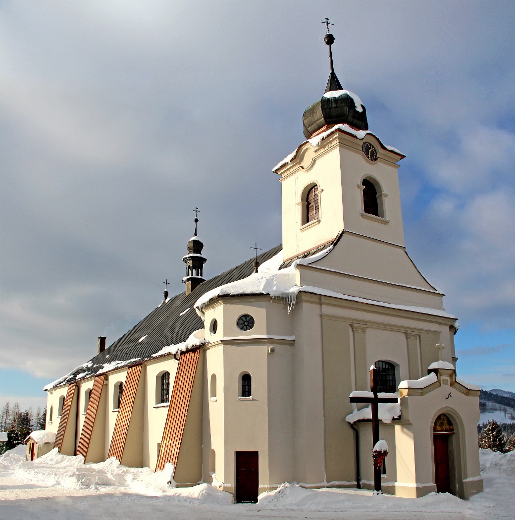 Murowany kościół zimą. Przed wejściem krzyż misyjny.