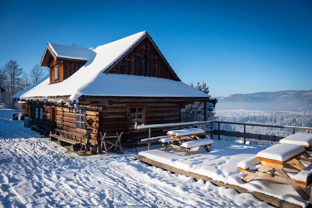Drewniany domek zimą, na drugim planie góry.